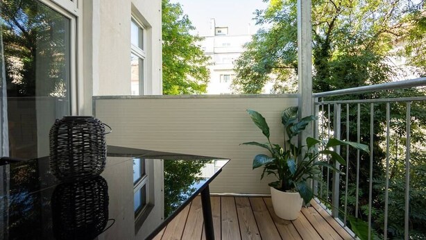 A balcony with a wooden floor, a potted plant, and a glass table with woven baskets. - Modern apartment with a balcony near Belvedere (Wien)