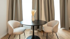 A room with two white armchairs, a round black table, and a vase with dried plants. - Modern apartment with a balcony near Belvedere (Wien)