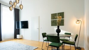 Un espace repas moderne avec une table ronde, des chaises recouvertes d’un tissu vert et un vase contenant des plantes séchées.