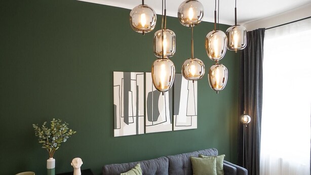 Un salon moderne avec un mur vert foncé, un canapé gris et une œuvre d’art abstraite originale.