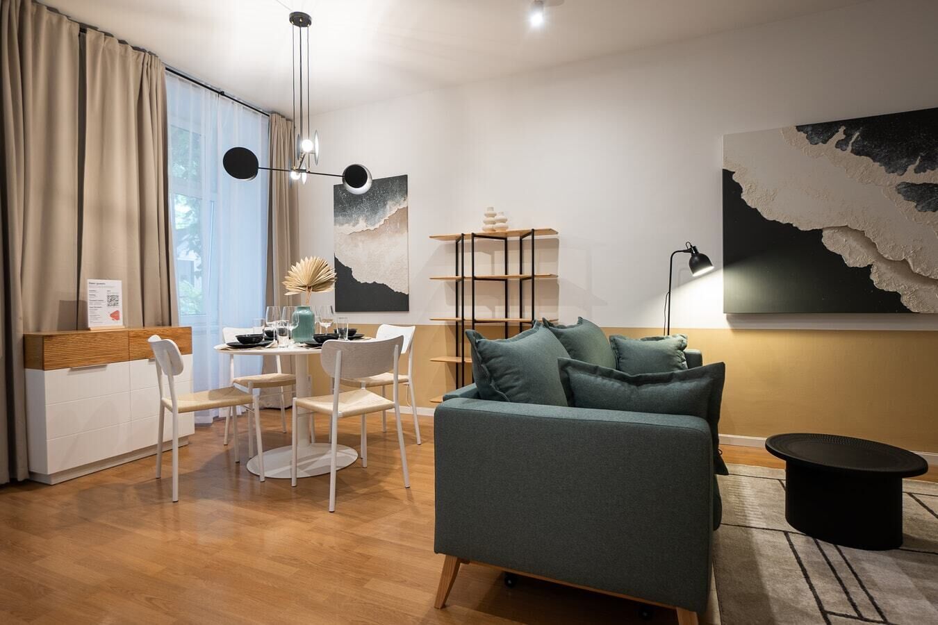 Ein modernes Wohnzimmer mit Sofa, Esstisch und Stühlen. Außerdem befindet sich ein Bücherregal und eine Lampe dort.