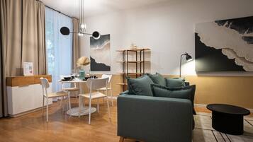 Ein modernes Wohnzimmer mit Sofa, Esstisch und Stühlen. Außerdem befindet sich ein Bücherregal und eine Lampe dort.