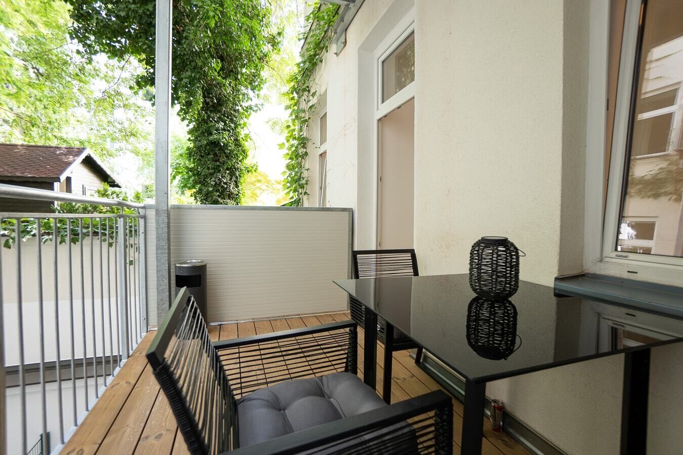 Ein Balkon mit einem Glastisch, schwarzen Stühlen und einer Korbusvase.
