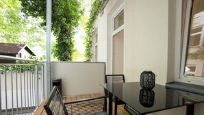 Un balcon avec une table en verre, des chaises noires et un vase en osier.