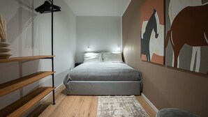 Ein Schlafzimmer mit Bett, Nachttisch, Wandlampe, Holzregal, Teppich und einem Gemälde.