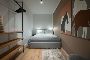 A bedroom with a bed, a nightstand, a wall-mounted light, a wooden shelf, a rug, and a painting. - 2-room apartment with a terrace and queen-size bed (Wien)