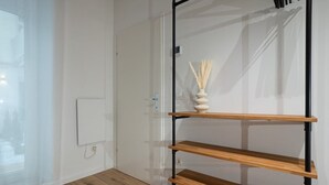 Ein Zimmer mit Holzboden, einer weißen Tür, einem an der Wand befestigten Regal mit einer Vase und einer Steckdose.