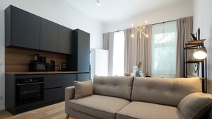 Ein modernes Wohnzimmer mit einer Couch, einer Küchenzeile mit dunklen Schränken und einem Esstisch mit einer Lampe.
