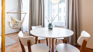 Een moderne eethoek met een ronde tafel, witte stoelen, een hangstoel en een vaas met takken.