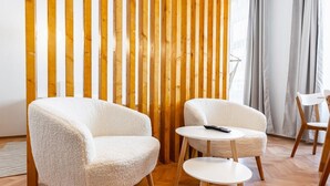 Een moderne woonkamer met twee witte fauteuils en een kleine witte tafel, houten latten op de muur, en een houten vloer.