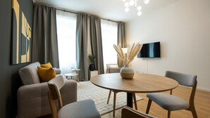 Una sala de estar moderna con una mesa redonda de madera, sofás grises y un televisor de pantalla plana montado en la pared.