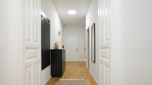 Un pasillo con paredes blancas, piso de madera, un mueble negro y una puerta al final.