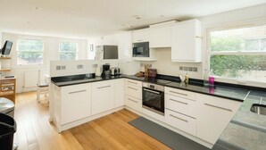 A modern kitchen with white cabinets, a black countertop, and a stainless steel refrigerator. - Elegant 4-Bed Islington Home with Garden (London)