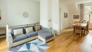 A modern living room with a sectional sofa, a dining table with chairs, a clock on the wall, and a geometric rug. - Elegant 4-Bed Islington Home with Garden (London)