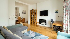 A modern living room with a sofa, a fireplace, a TV, and a bookshelf. - Elegant 4-Bed Islington Home with Garden (London)