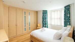 A bedroom with a large bed, wooden wardrobe, and a chair. - Elegant 4-Bed Islington Home with Garden (London)