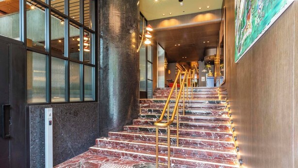 Un escalier avec des marches en marbre et des rampes dorées, menant à une pièce dotée d’une moquette rouge et d’une grande fenêtre.