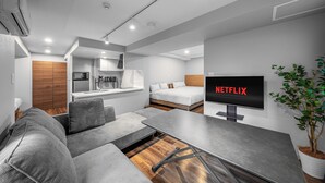 Um espaço de estar moderno e compacto, com cozinha compacta, sofá, mesa de jantar e TV exibindo o logotipo da Netflix.