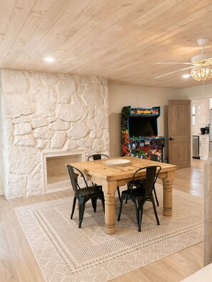 A dining area with a stone wall, a wooden table, black chairs, a patterned rug, and a colorful arcade machine. - Single Level Luxe Mtn Home w/Arcade, Hot Tub, Fire Pit and Grill (Gatlinburg)