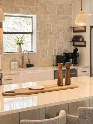 A kitchen with a stone wall, a window with a plant, a coffee machine, and wooden salt and pepper shakers on a cutting board. - Single Level Luxe Mtn Home w/Arcade, Hot Tub, Fire Pit and Grill (Gatlinburg)