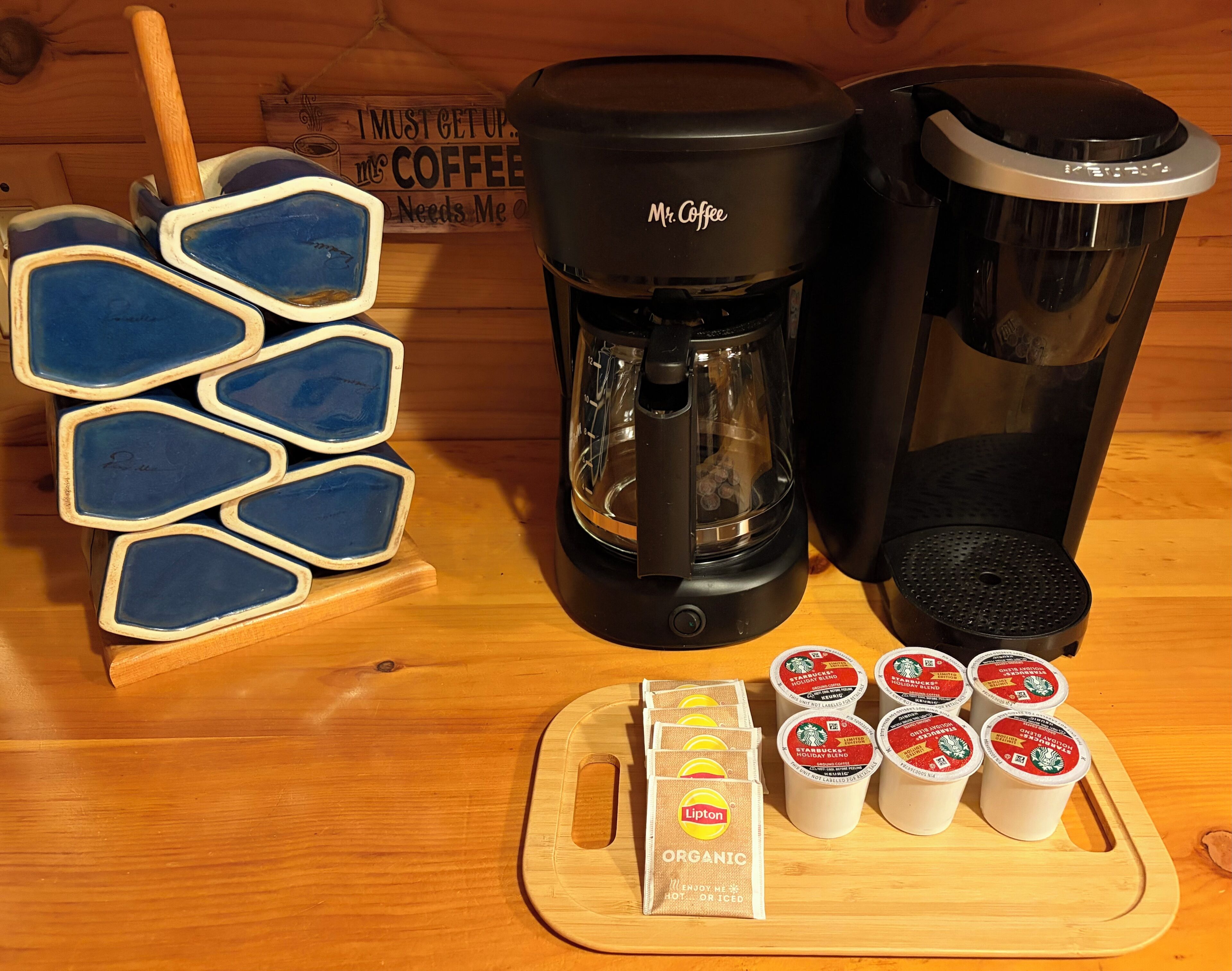A coffee maker, a coffee pot, a tray with Lipton tea bags, and a wooden sign with a coffee theme.