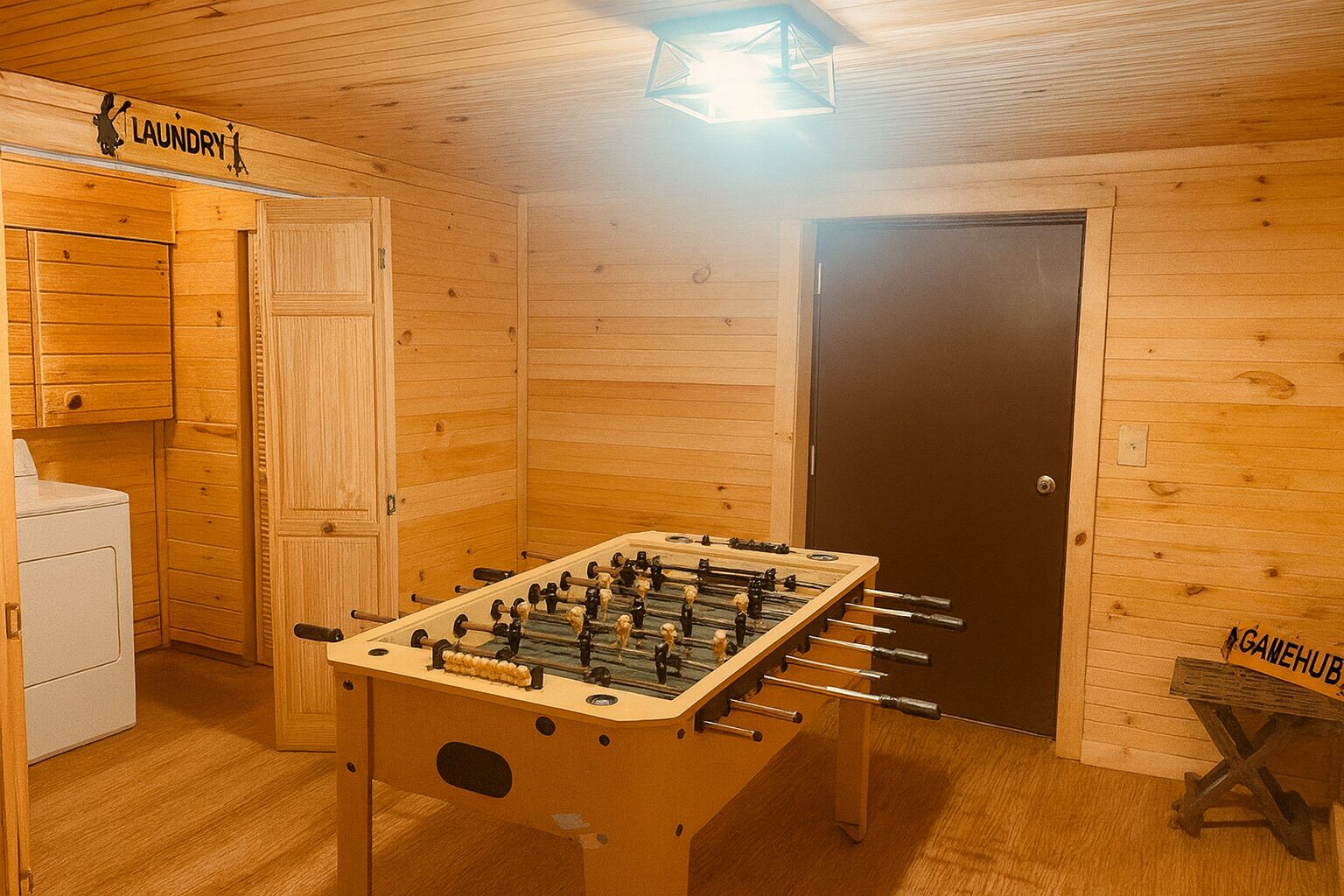 Habitació amb interior de fusta, taula de futbolí, zona de bugaderia i una porta amb la inscripció 'GAMEHUB'.