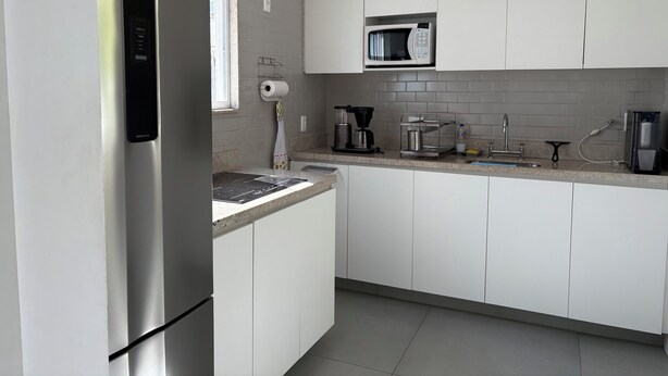 A modern kitchen with white cabinets, a stainless steel refrigerator, a microwave, and a coffee maker. - Retreat with a view of Christ the Redeemer, South Zone of Rio de Janeiro (Rio de Janeiro)