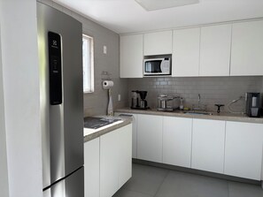 Eine moderne Küche mit weißen Schränken, einem Edelstahl-Kühlschrank, einer Mikrowelle und einer Kaffeemaschine.