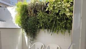 A balcony with a white tiled wall, two white plastic chairs, and a variety of green plants including ferns and flowering plants. - Retreat with a view of Christ the Redeemer, South Zone of Rio de Janeiro (Rio de Janeiro)