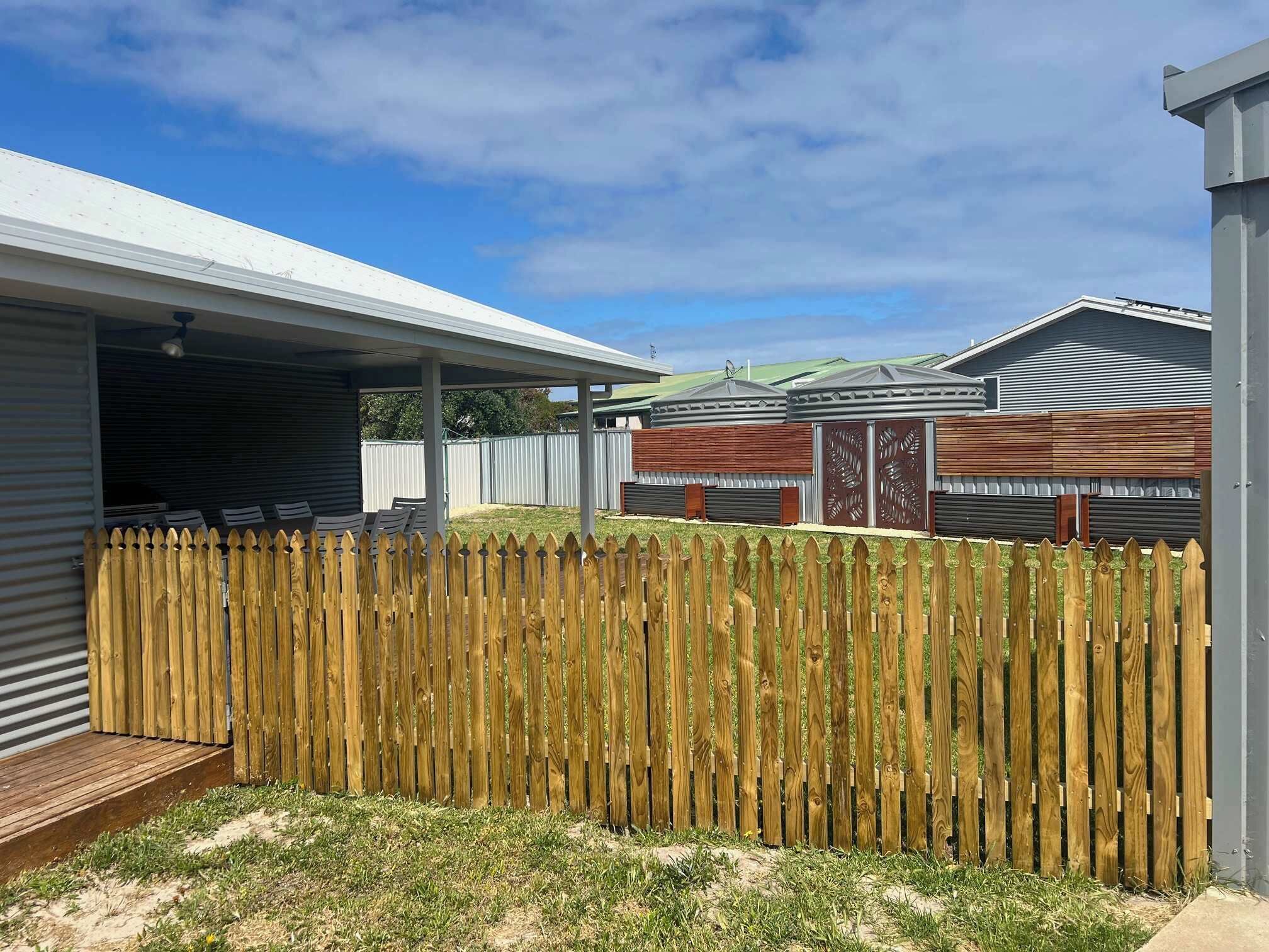Un quartier résidentiel avec une clôture en bois, un patio couvert et, au fond, un bâtiment en métal.