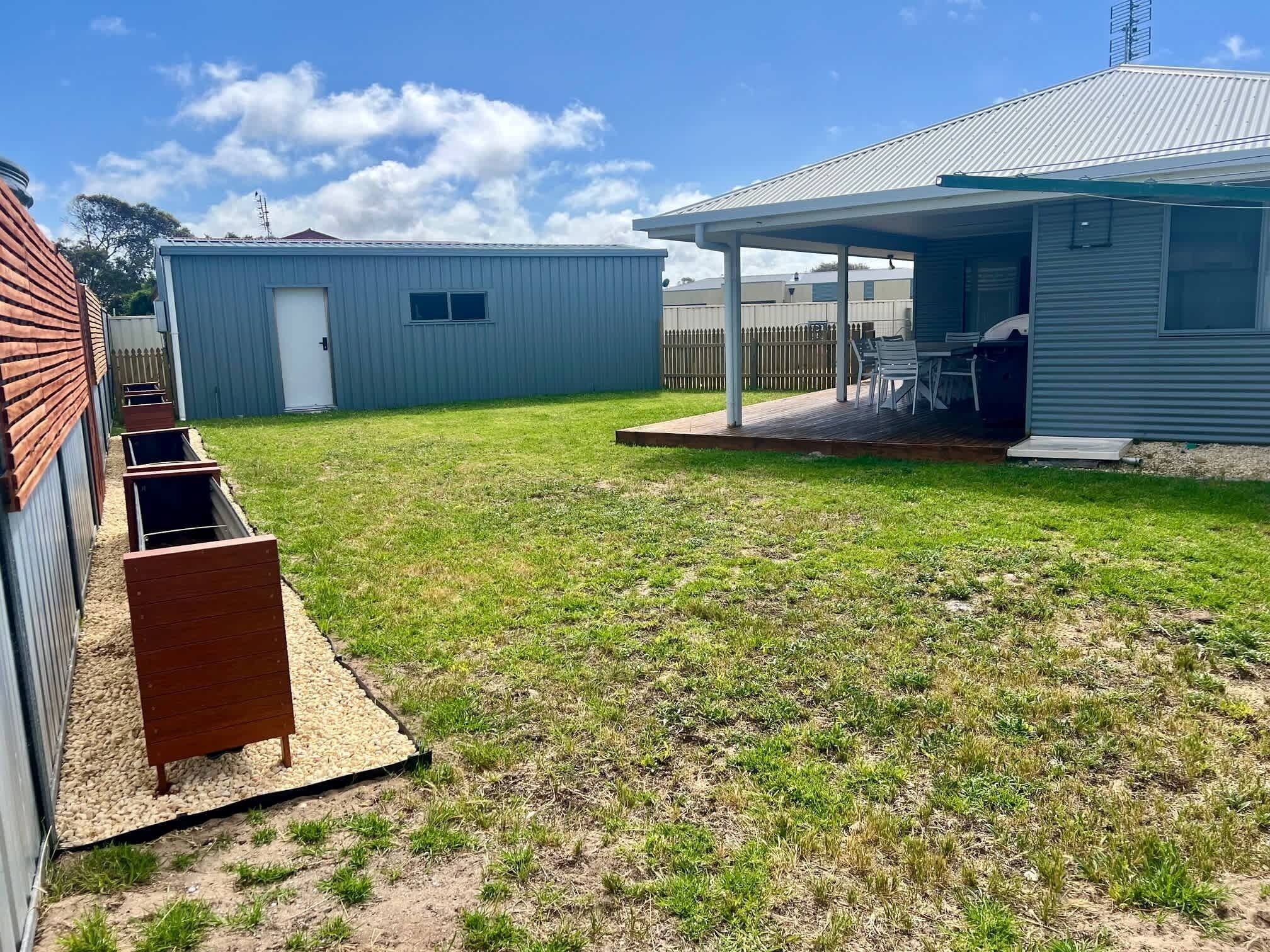 Un jardin avec un espace barbecue, une terrasse couverte et un abri de jardin.