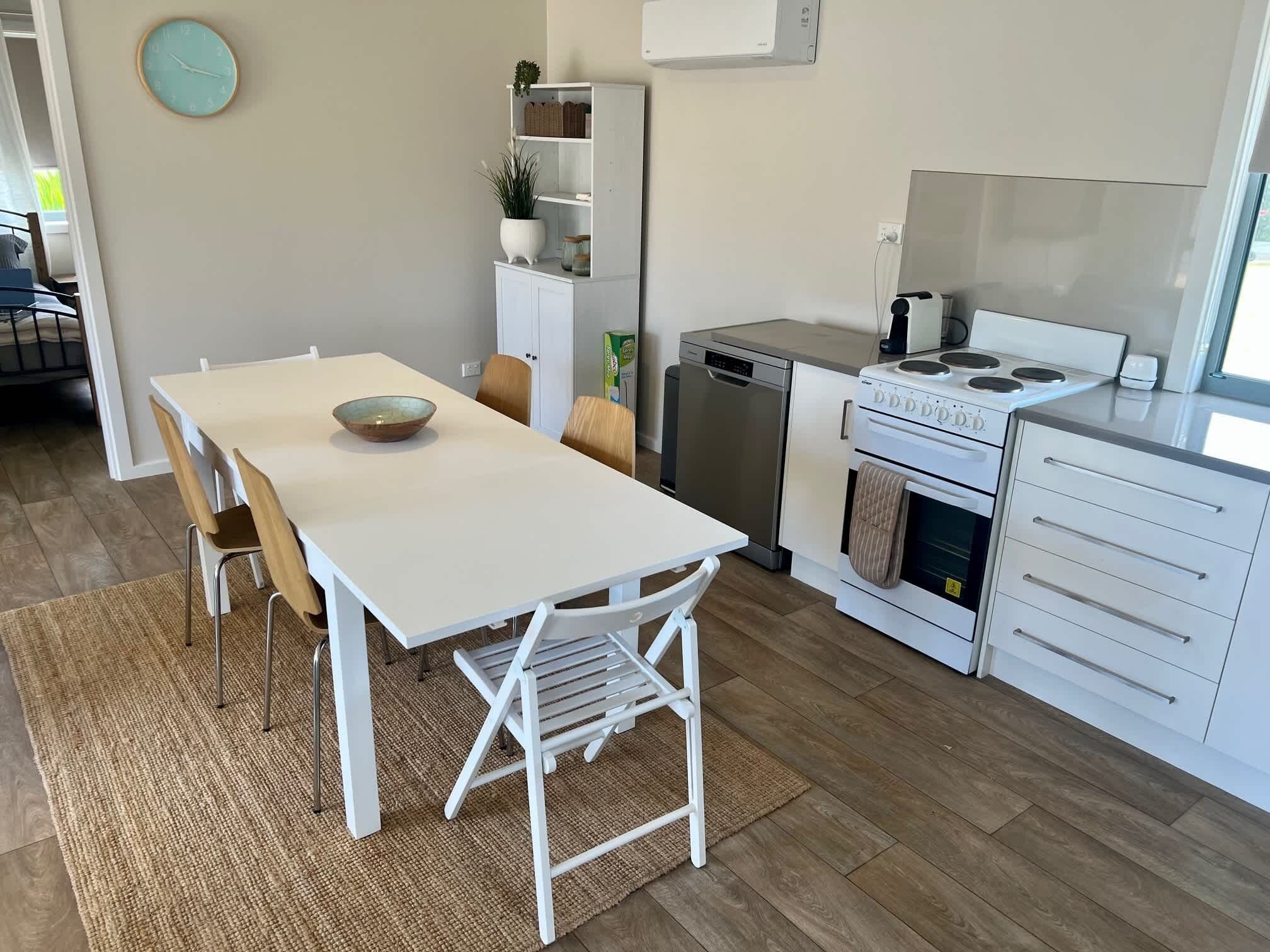 Een moderne keuken met witte kasten, een eettafel met stoelen, een inbouwoven en een vaatwasser.