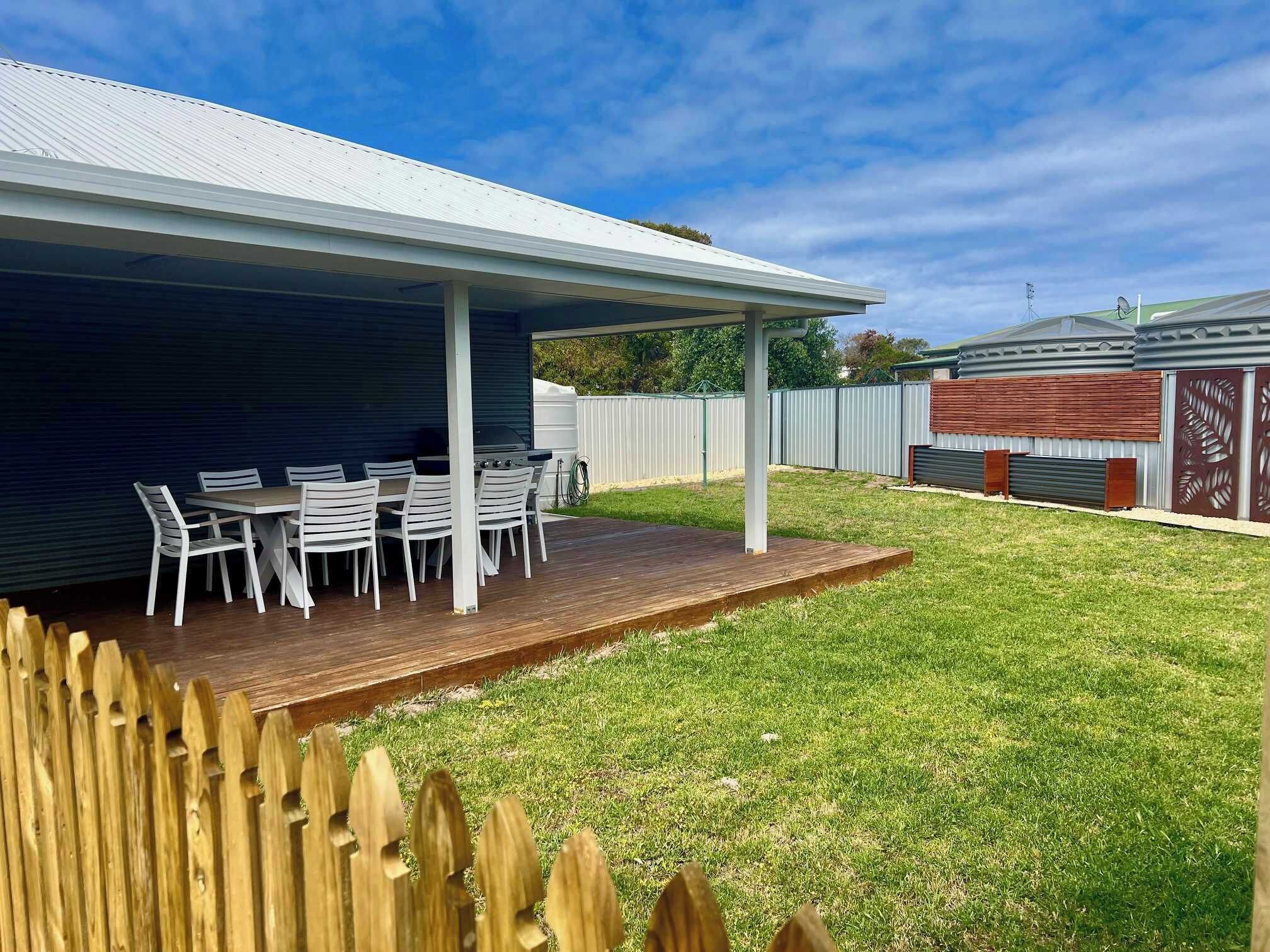 Un patio couvert avec une table et des chaises, une terrasse en bois et une cour clôturée.