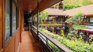 A wooden corridor with a view of a garden area, a sign reading "HOMESTAY MAI CHAUMOMEN," and a building with a tiled roof. - Home Stay Mai Châu Moment (Mai Ha)
