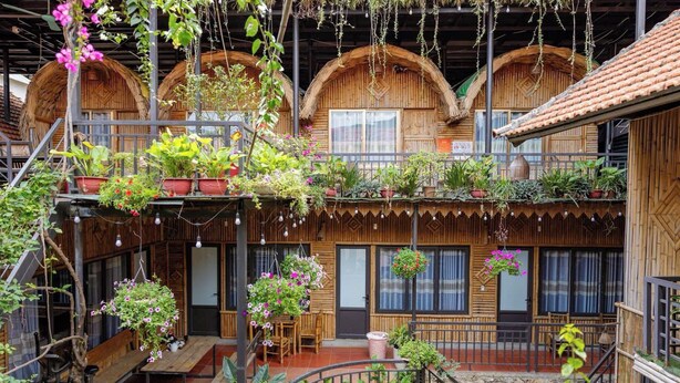 A wooden building with multiple balconies, each adorned with hanging plants and potted flowers. - Home Stay Mai Châu Moment (Mai Ha)