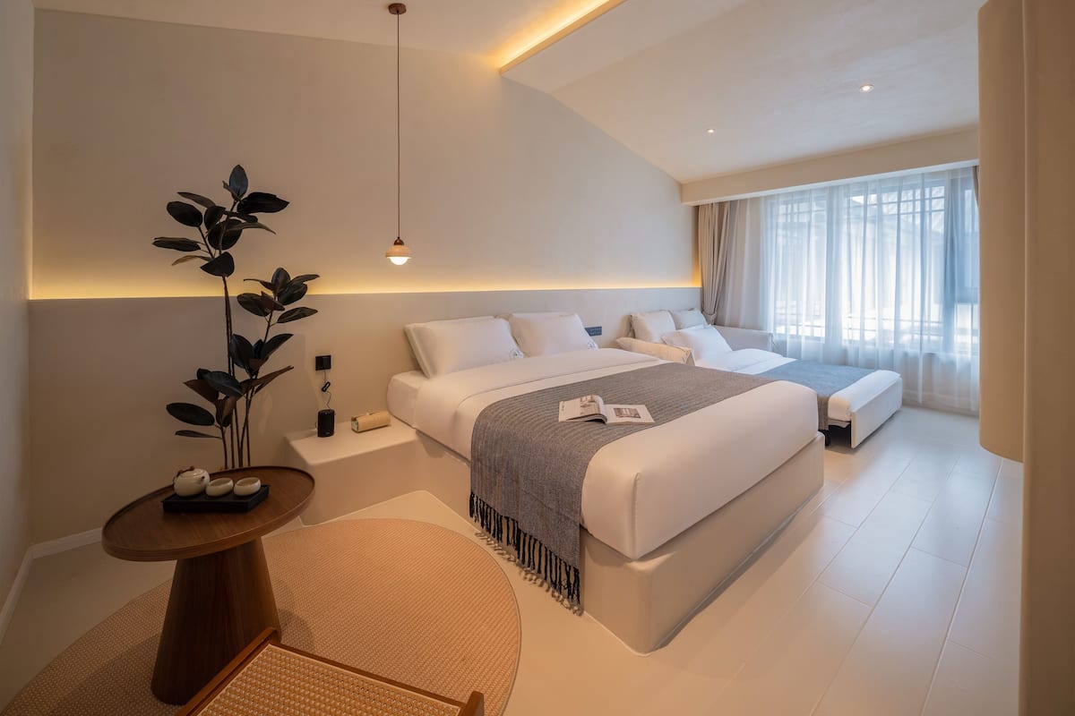 Un dormitorio moderno con una cama grande, mesitas de noche, una pequeña mesa redonda y una planta en maceta.