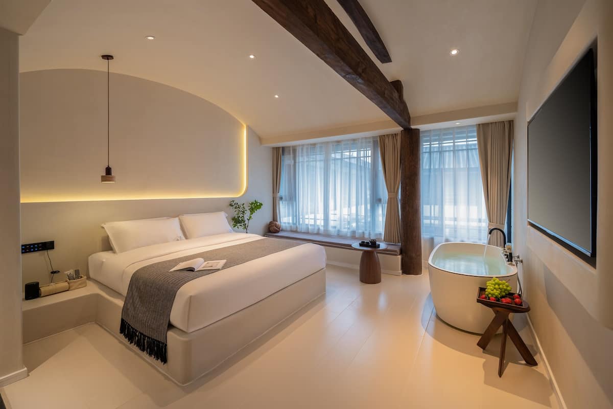 Un dormitorio moderno con una cama grande, una bañera integrada y un ventanal con cortinas.