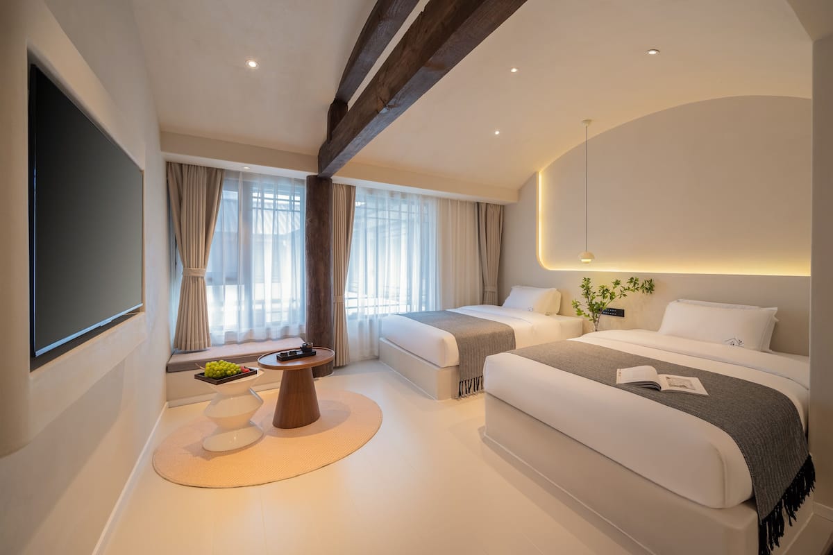 Una habitación de hotel moderna con una cama grande, una cama más pequeña, un televisor de pantalla plana y un área de comedor con una mesa y sillas.