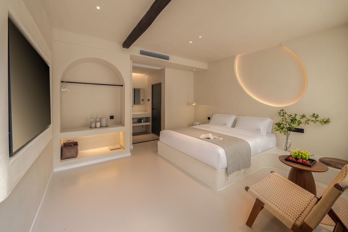 Un dormitorio moderno con una cama grande, mesitas de noche, un televisor y un pequeño comedor con una mesa y sillas.