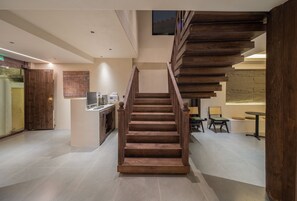 A modern interior with a wooden staircase leading to a second floor, a kitchen area, and a seating area with a table and chairs. - Yijianju Garden Inn (Lijiang)