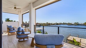 Ein Balkon mit zwei blauen Sitzgelegenheiten, einem kleinen Tisch und Blick auf eine Marina mit Booten und Palmen.