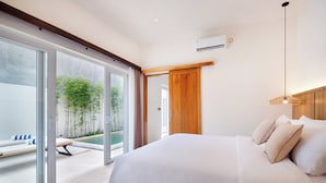 Ein modernes Schlafzimmer mit einem großen Bett, Schiebegläsern, die zum Poolbereich führen, und einem Holzbalken an der Decke.