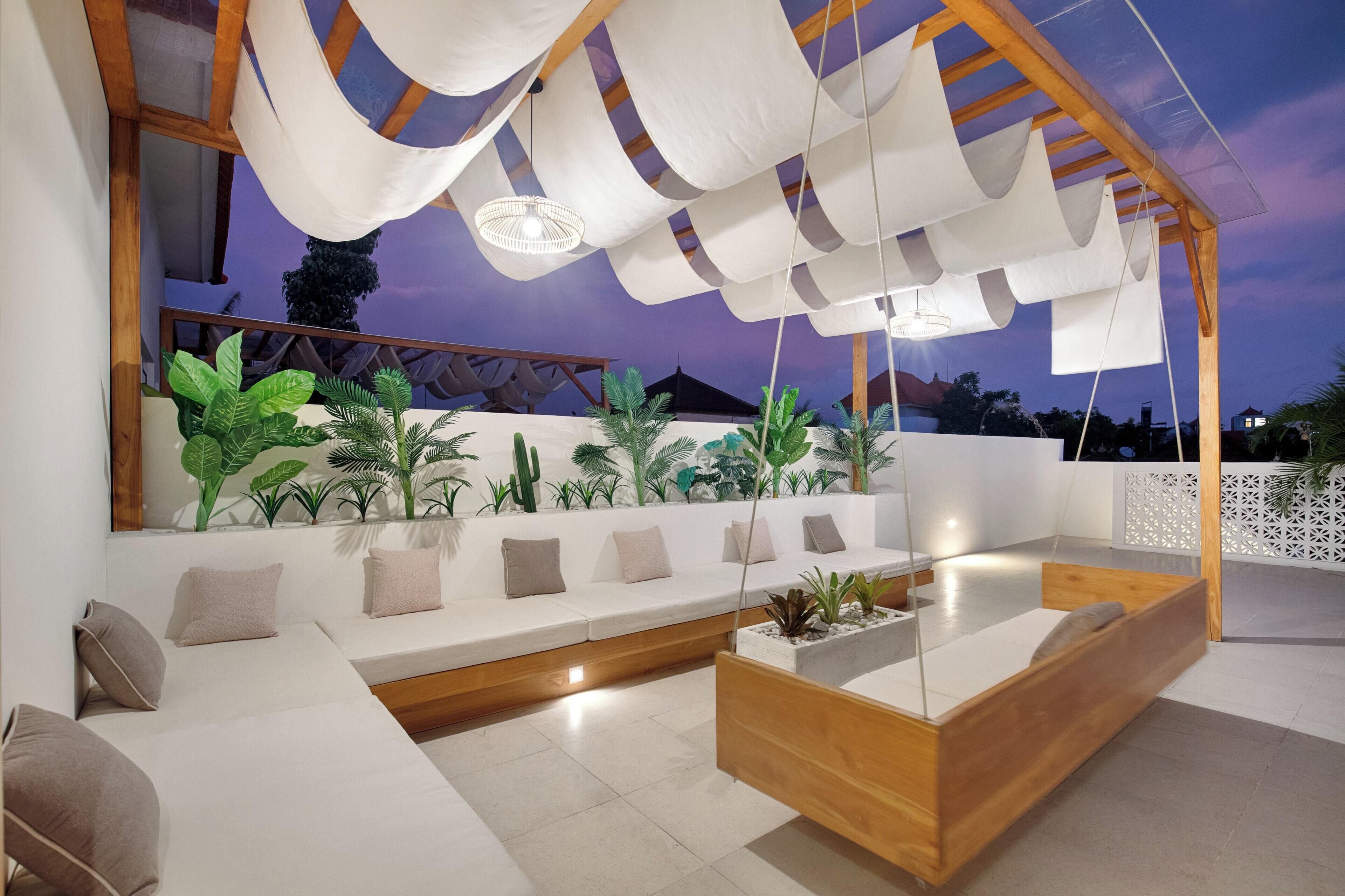 A modern outdoor seating area with a wooden bench, white cushions, and hanging fabric structures.