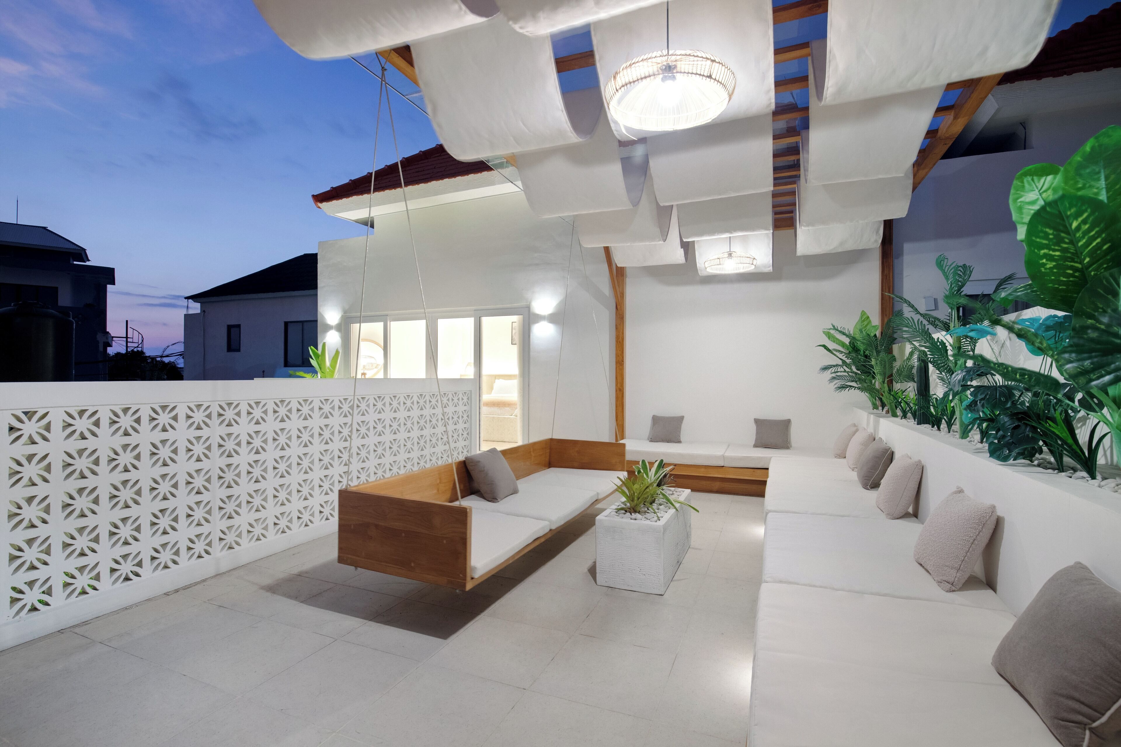 Un área de estar exterior moderna con un banco de madera, un sofá blanco y una jardinera con plantas verdes.