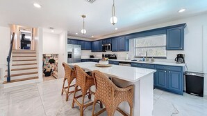 A modern kitchen with blue cabinets, a white island, and wicker bar stools.