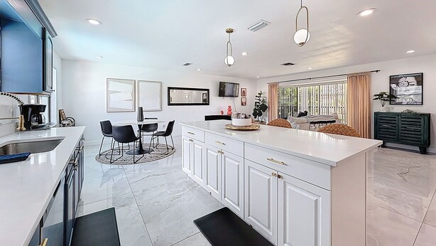A modern kitchen with white cabinetry, a central island, and a dining area with black chairs.