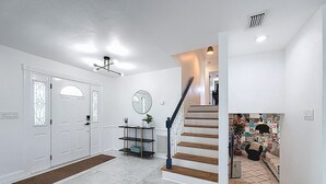 A modern interior with a staircase, a hallway, and a door with a decorative glass panel.