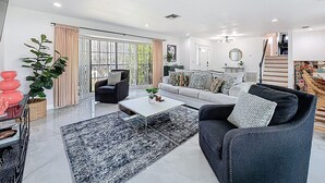 A modern living room with a sofa, armchairs, a coffee table, and a large window with curtains.