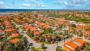 Ett bostadsområde med hus som har orangefärgade tak, palmer och en fri utsikt över havet.