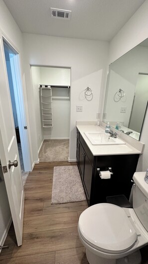 Un baño con inodoro blanco, lavamanos con espejo y un perchero para toallas.